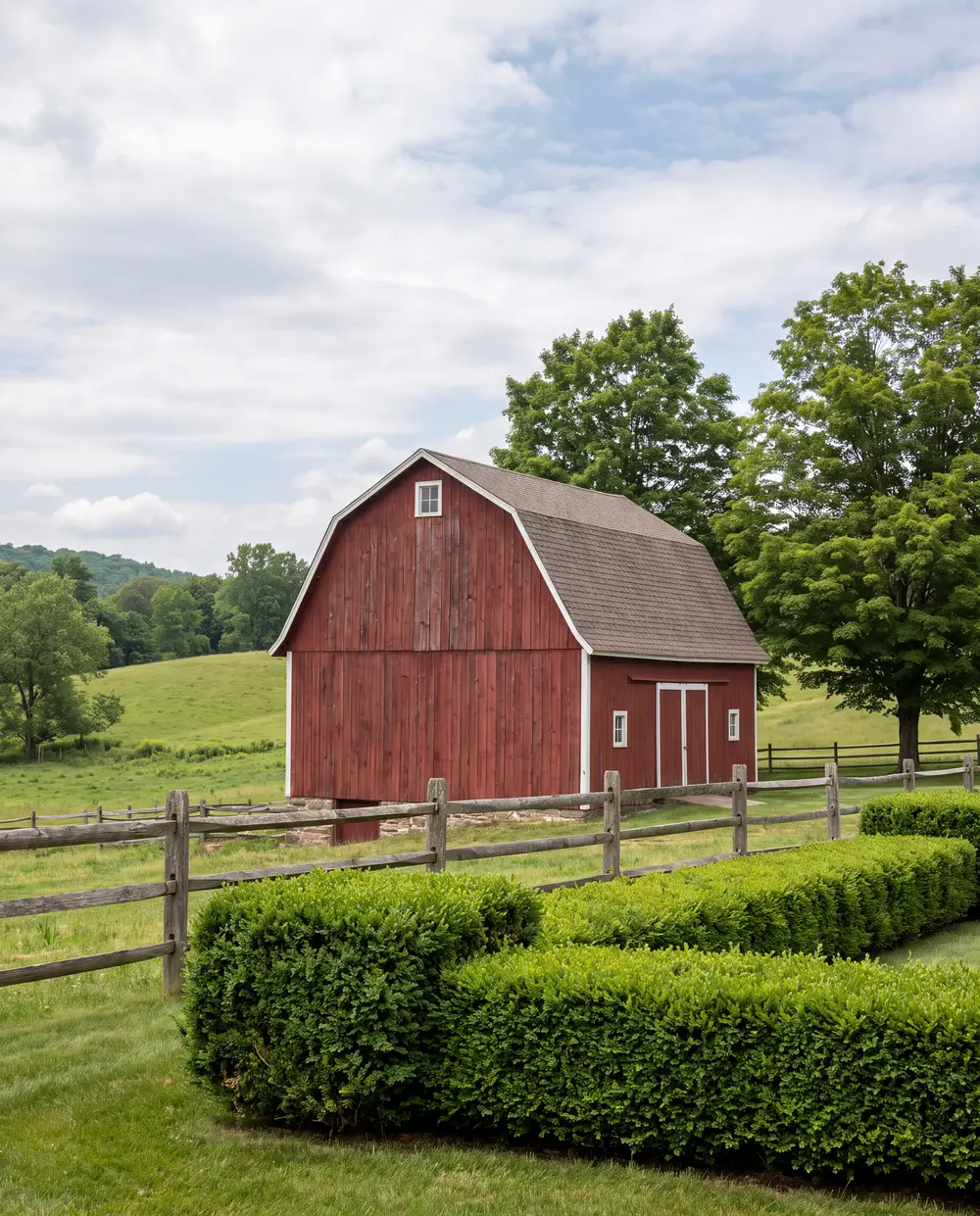 Neatly trimmed hedges and a split-rail fence in front of a red New England barn