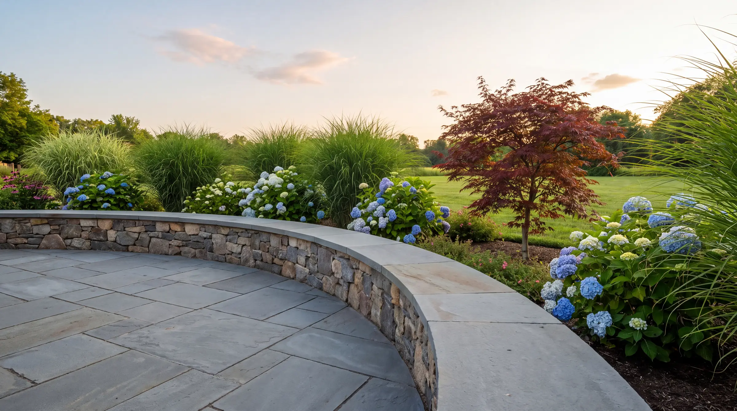Newly designed backyard with a bluestone patio, layered planting beds and a stone seat wall